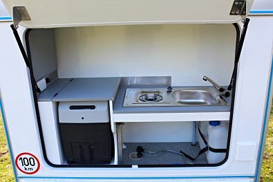 Kuchyňka s lednicí a dřezem a plynovým vařičem v karavanu Tomplan
